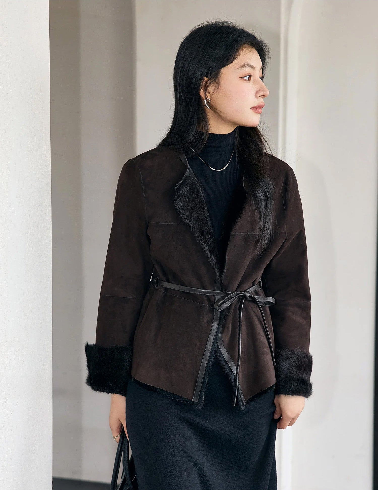 Model holding a bag and looking out the window in the Tamarind goatskin jacket with visible leather trims — From Borcelleclothes.
