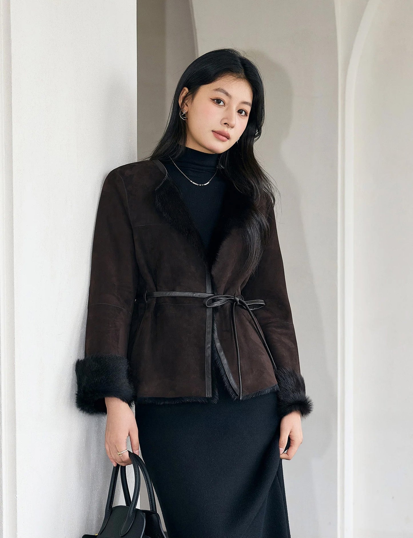 Model leaning against a white wall in the Tamarind goatskin jacket, revealing the natural drape of suede — From Borcelleclothes.