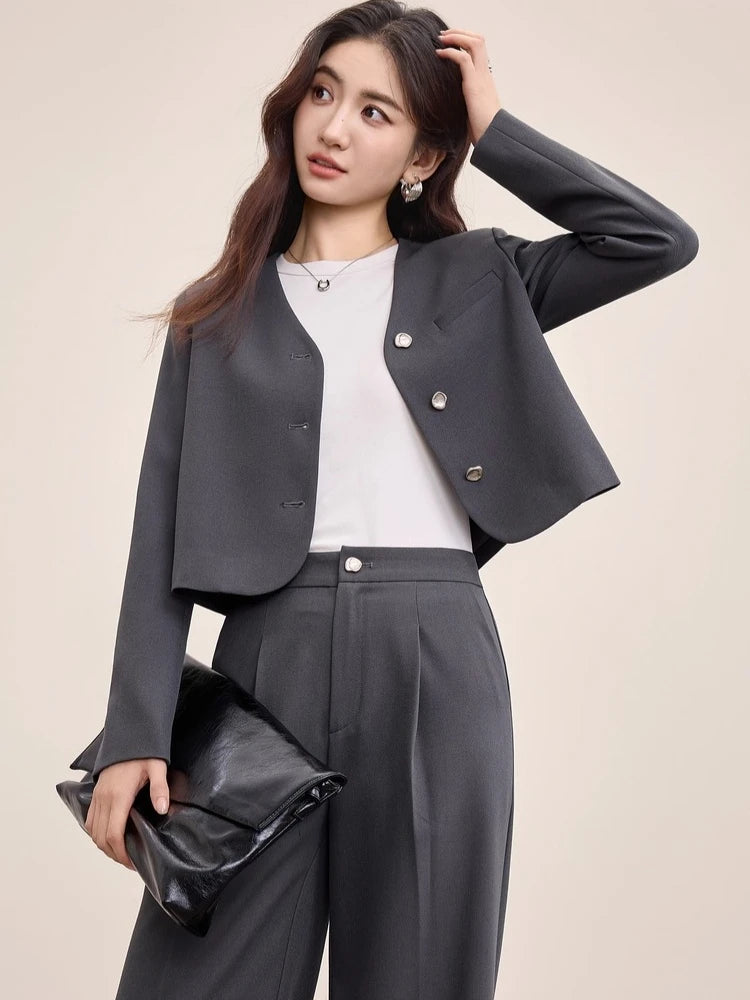 A relaxed moment of a woman in an unfastened Gris Phénix suit, touching her hair with effortless grace — From Borcelleclothes.