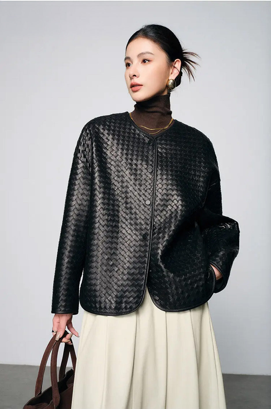Detail view of model holding bag with hand in skirt pocket wearing woven nappa jacket — From Borcelleclothes.