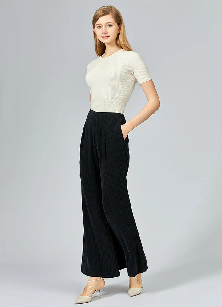Model turned slightly to the side showing the silhouette of women's pinstripe silk trousers — From Borcelleclothes.