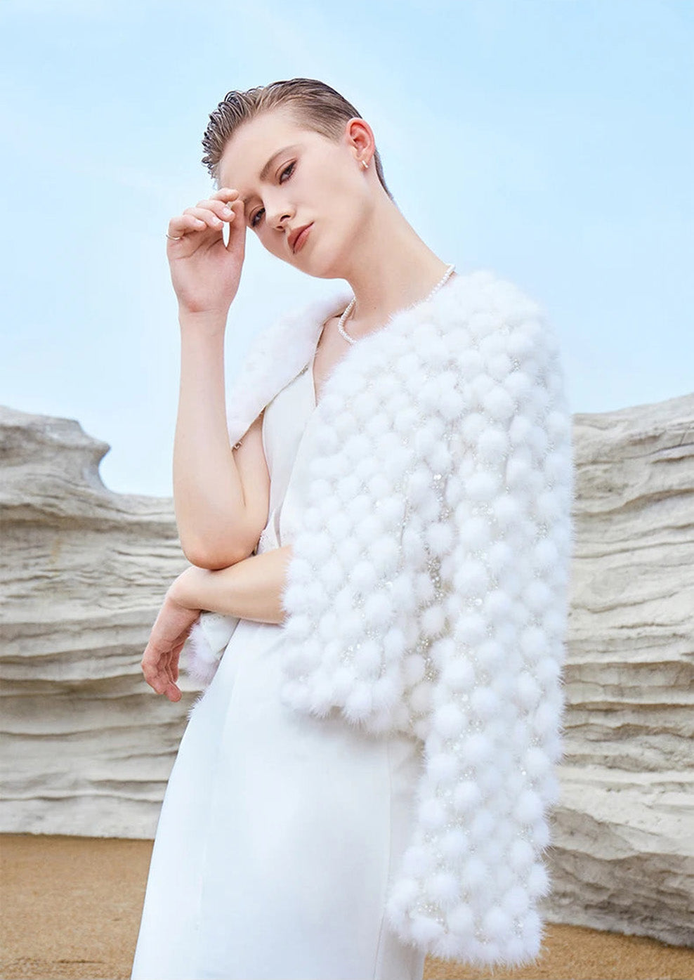 Model gently touching her eyebrow in the White Whimsy mink mosaic coat, accentuating texture — From Borcelleclothes.