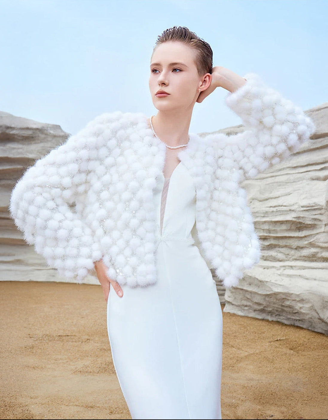 Model touching her hair while wearing the Women’s Inlaid Mink Mosaic Coat in White Whimsy, showing soft pom-pom texture — From Borcelleclothes.