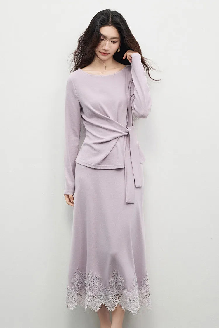 A woman in an Almost There knit set softly adjusting her hair, highlighting the boatneck and the central origami knot. — From Borcelleclothes.