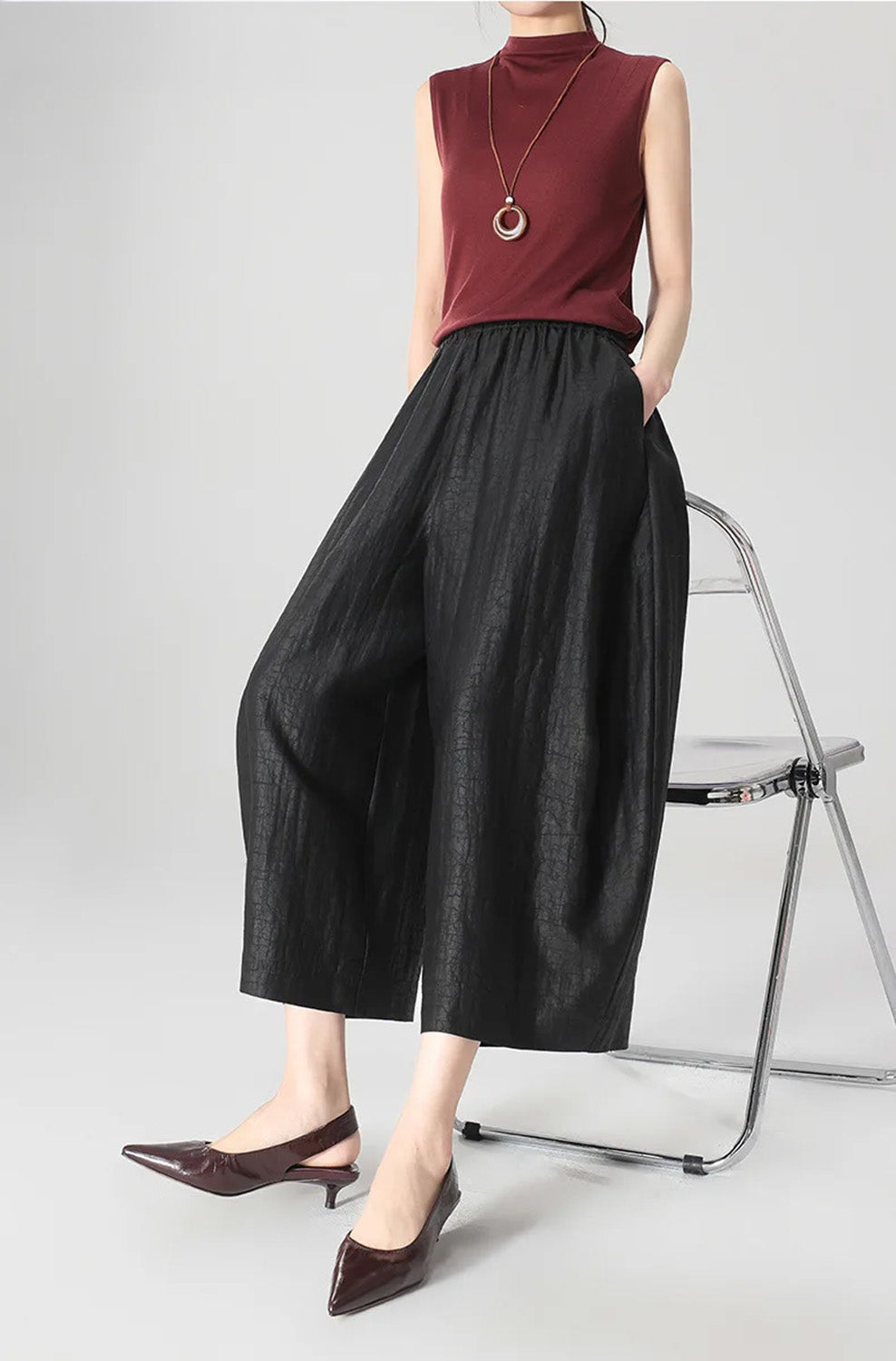A woman perching on the back of a chair wearing black Xiangyunsha Mulberry silk lantern pants in Tortoise Ticket — From Borcelleclothes.