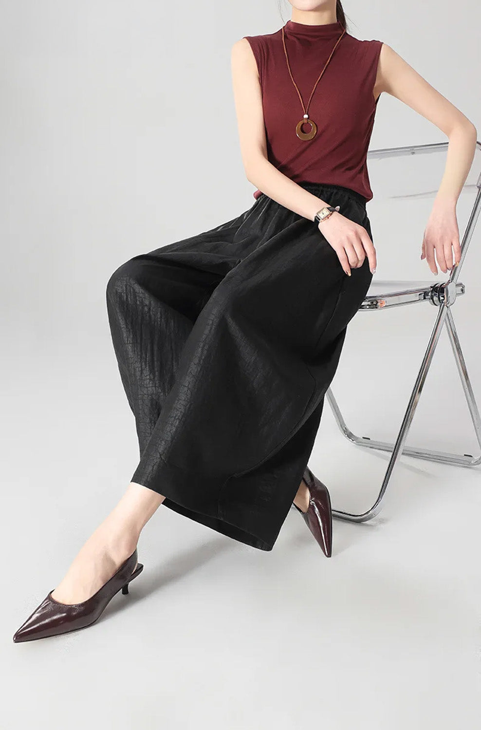 A woman sitting on the edge of a chair wearing black Xiangyunsha Mulberry silk lantern pants in Tortoise Ticket — From Borcelleclothes.