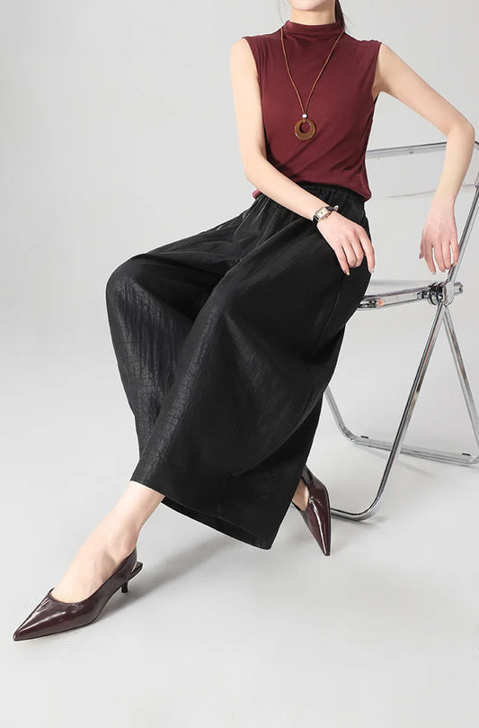 A woman sitting on the edge of a chair wearing black Xiangyunsha Mulberry silk lantern pants in Tortoise Ticket — From Borcelleclothes.