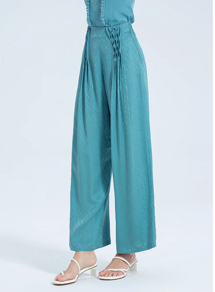 Woman wearing wide-leg Lapis Waters Mulberry silk trousers with hand-tacked lattice pleats, turned slightly to the side to showcase the fluid jacquard texture. — From Borcelleclothes.