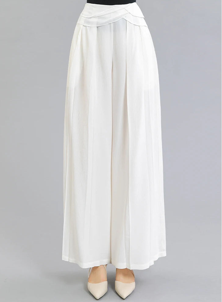 Front view of a woman wearing No Reward Mulberry silk trousers featuring front knife pleats and draped overlays — From Borcelleclothes.