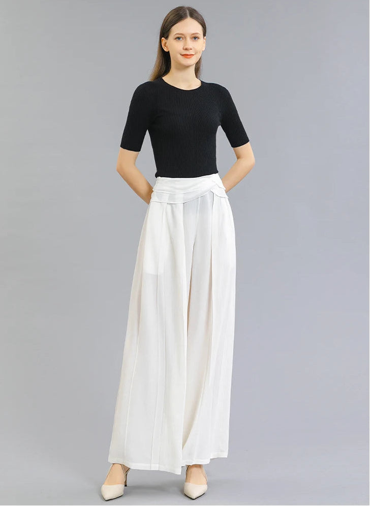Full-length view of a woman wearing Mulberry silk wide-leg trousers in No Reward, standing with hands behind her back — From Borcelleclothes.