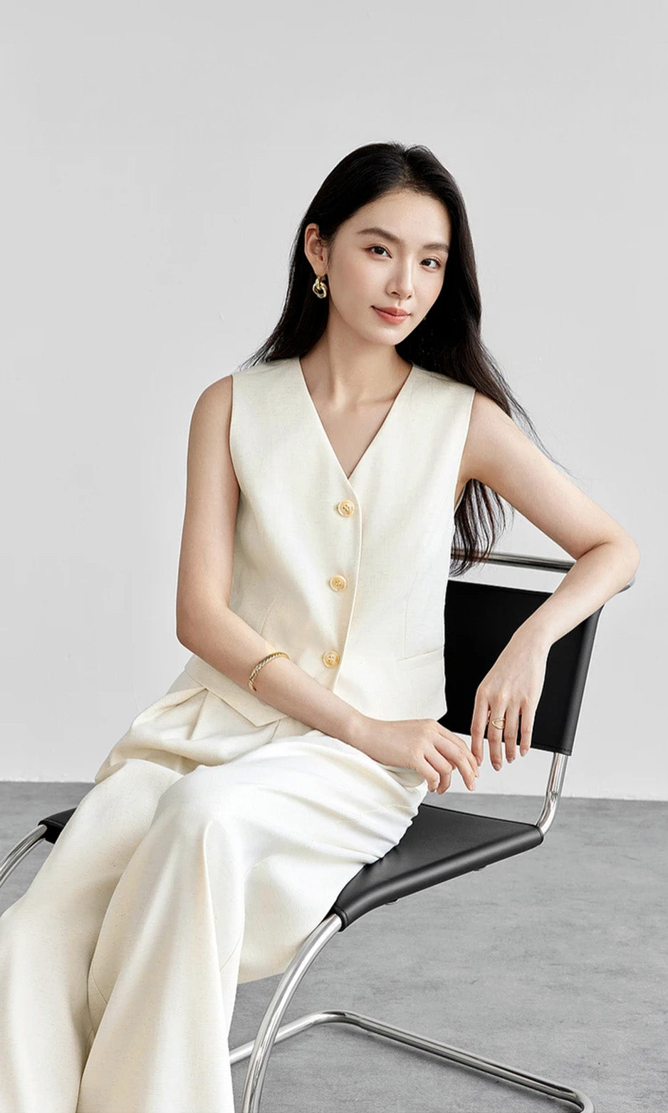 Woman sitting in a chair wearing a cream linen blend vest and wide-leg trousers. From Borcelleclothes.