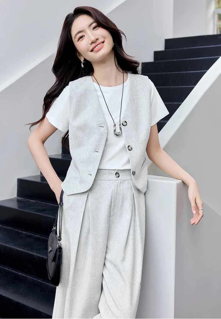 Woman in a gray linen blend set leaning against a stone stairs parapet. From Borcelleclothes.