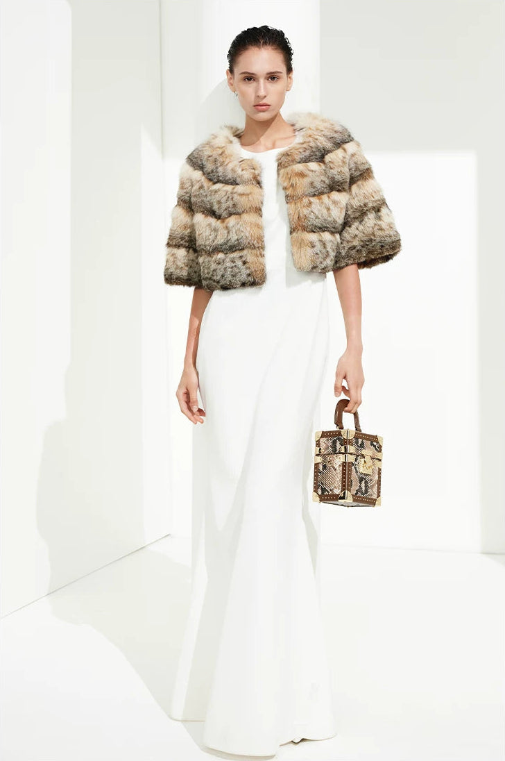 Full-length portrait of a woman styling the cropped bobcat cape with a fluid white dress and leather bag — From Borcelleclothes.