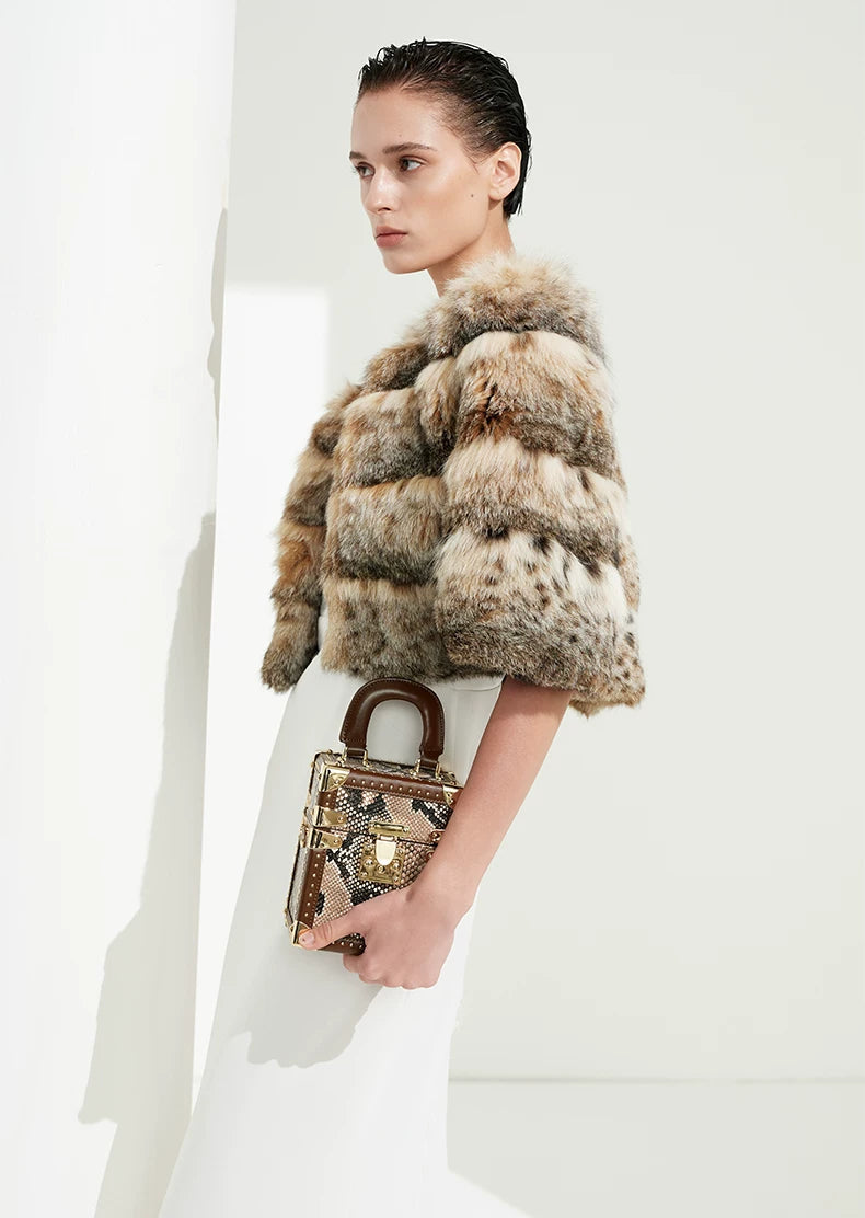 Poised woman standing in front of a sculptural white column wrapped in rare North American lynx fur — From Borcelleclothes.