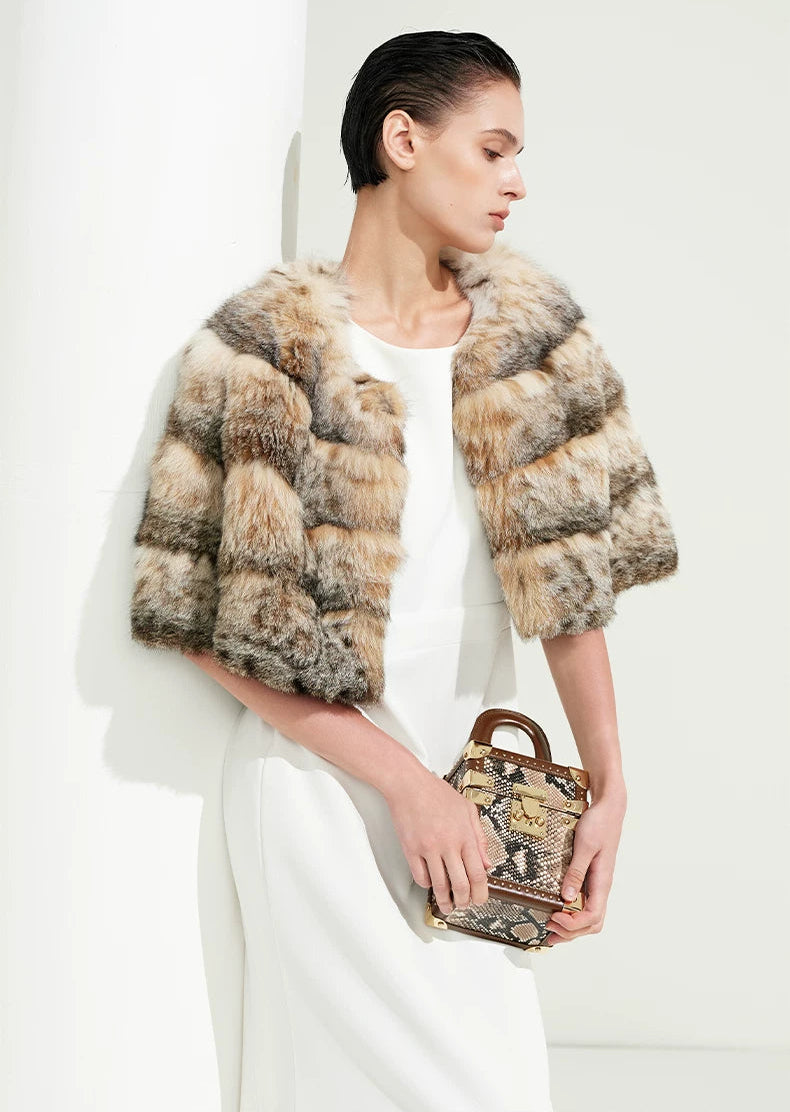 Confident woman posing gracefully beside classical white columns in a cropped amber lynx fur cape — From Borcelleclothes.