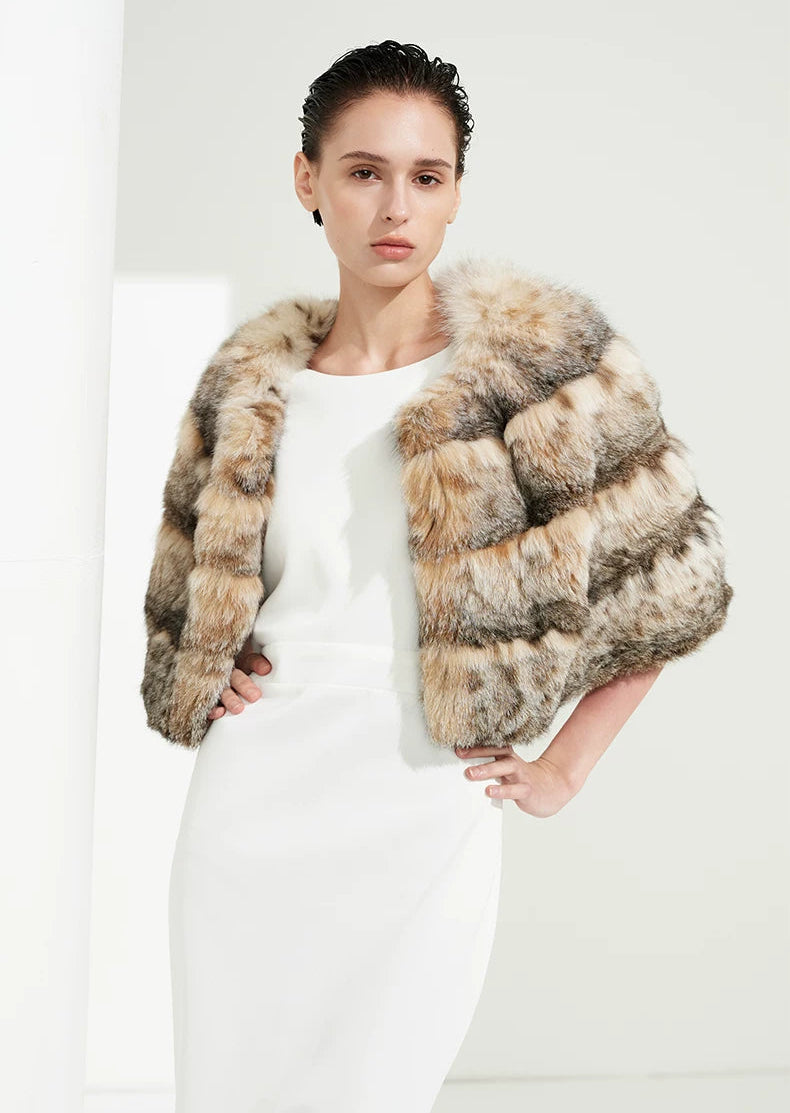Women's Handcrafted cropped lynx cape in natural amber tones. Features certified North American bobcat fur, horizontal paneling, pure silk lining, and concealed closure. — From Borcelleclothes.