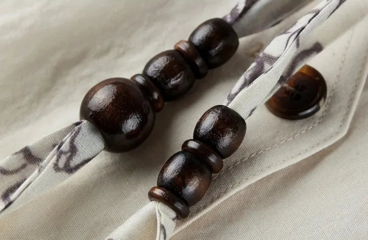 Detailed view of the warm wooden sphere and ring beads on the ribbon — From Borcelleclothes.