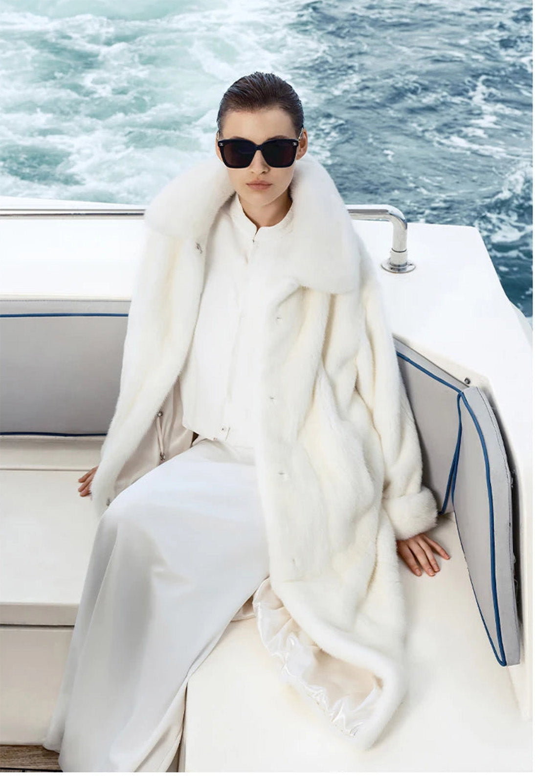 Women’s minimalist mink coat in White Echo, model seated on yacht bench, coat draped open over full-length white look. — From Borcelleclothes.