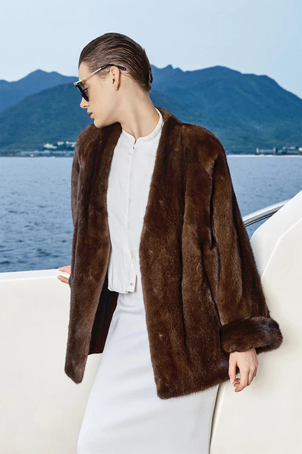 Model in Trace of Clove mink coat gazing toward the sea, V-shaped neckline visible — From Borcelleclothes.