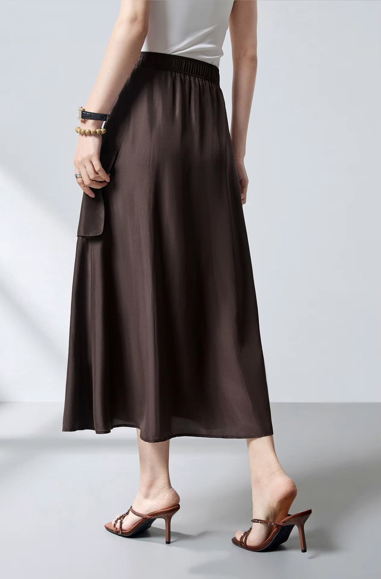 Back view of a model wearing a flared silk cargo skirt in Bitter Chocolate, showing the comfortable elasticated waistband — From Borcelleclothes.