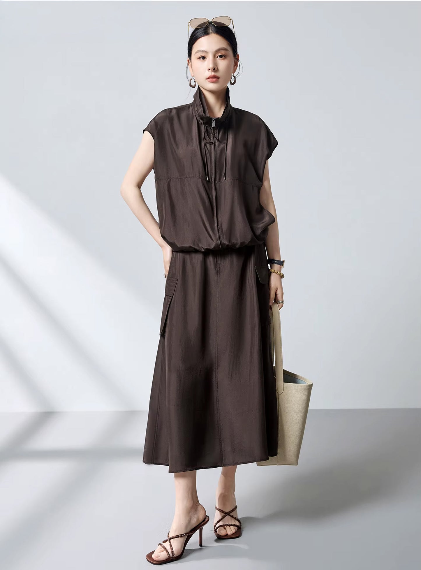 Model wearing a Bitter Chocolate silk cargo skirt and matching top, holding a large beige oversized tote bag — From Borcelleclothes.