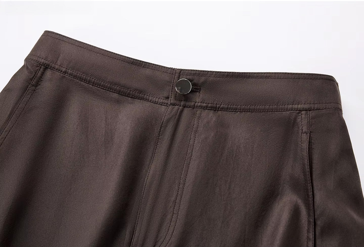 Close-up of the front waistband of a Bitter Chocolate silk cargo skirt, featuring a structured zipper fly and a polished stone-effect button — From Borcelleclothes.