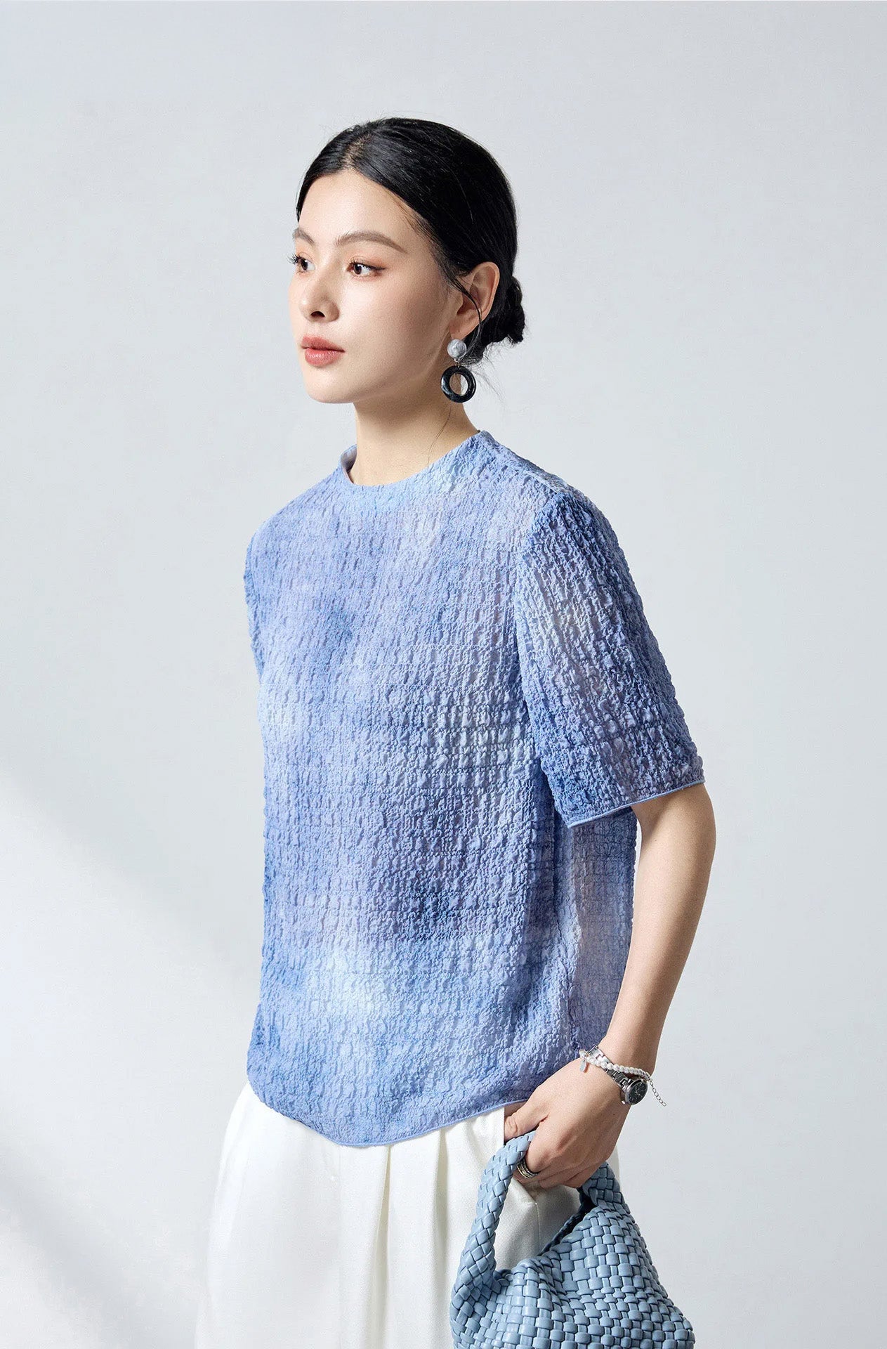 Model holding a woven bag turned slightly to the side in the Cloudy Sky silk jacquard top — From Borcelleclothes.