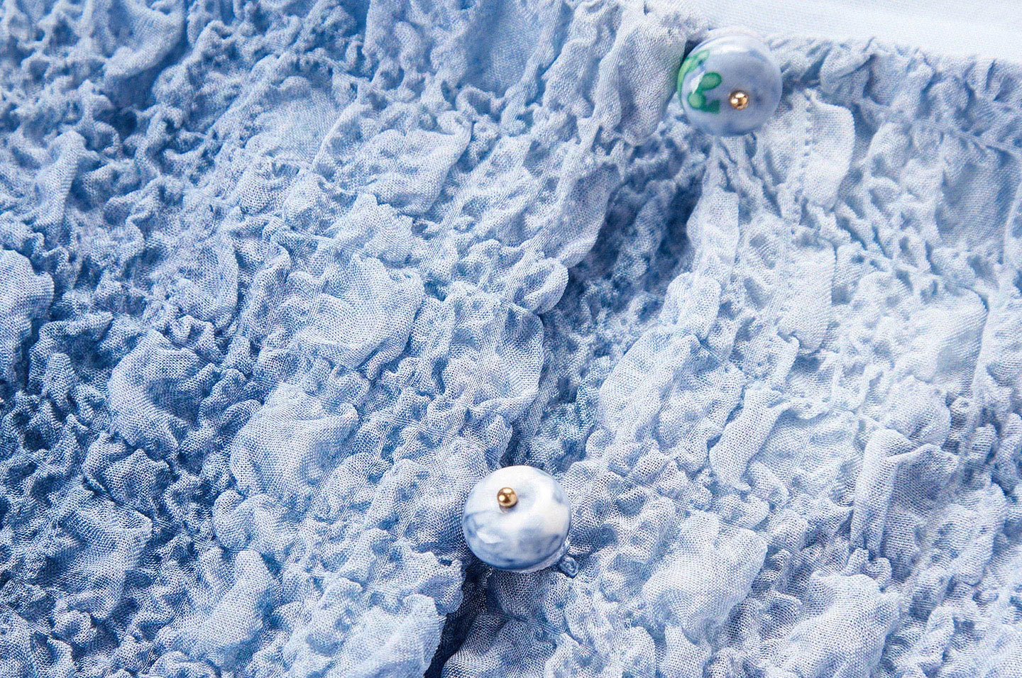 Macro view of the two hand-painted porcelain bead buttons and rouleau loops on the Cloudy Sky top — From Borcelleclothes.