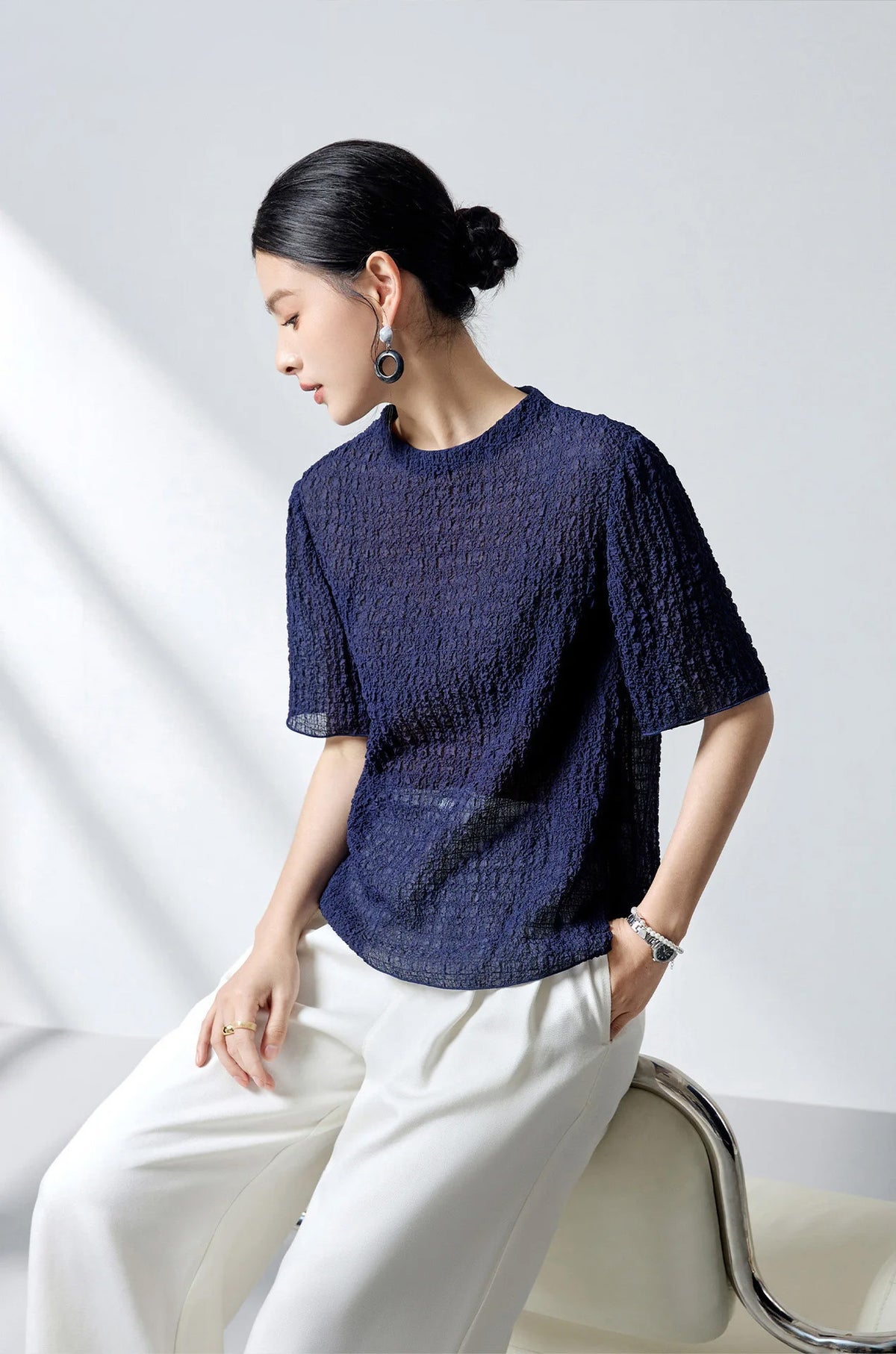 Model perching on a chair back wearing the Sagittarius mulberry silk puckered jacquard top — From Borcelleclothes.