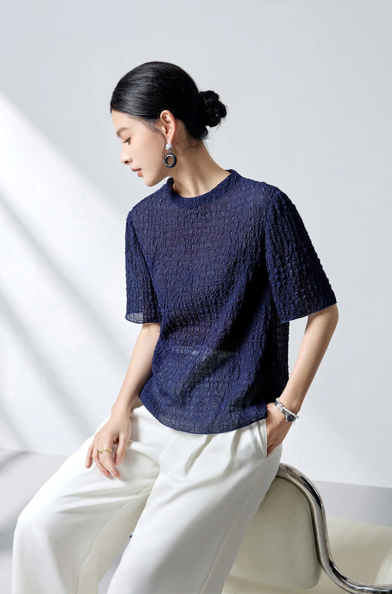 Model perching on a chair back wearing the Sagittarius mulberry silk puckered jacquard top — From Borcelleclothes.