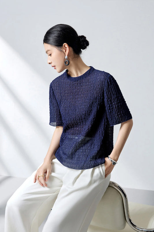 Model perching on a chair back wearing the Sagittarius mulberry silk puckered jacquard top — From Borcelleclothes.