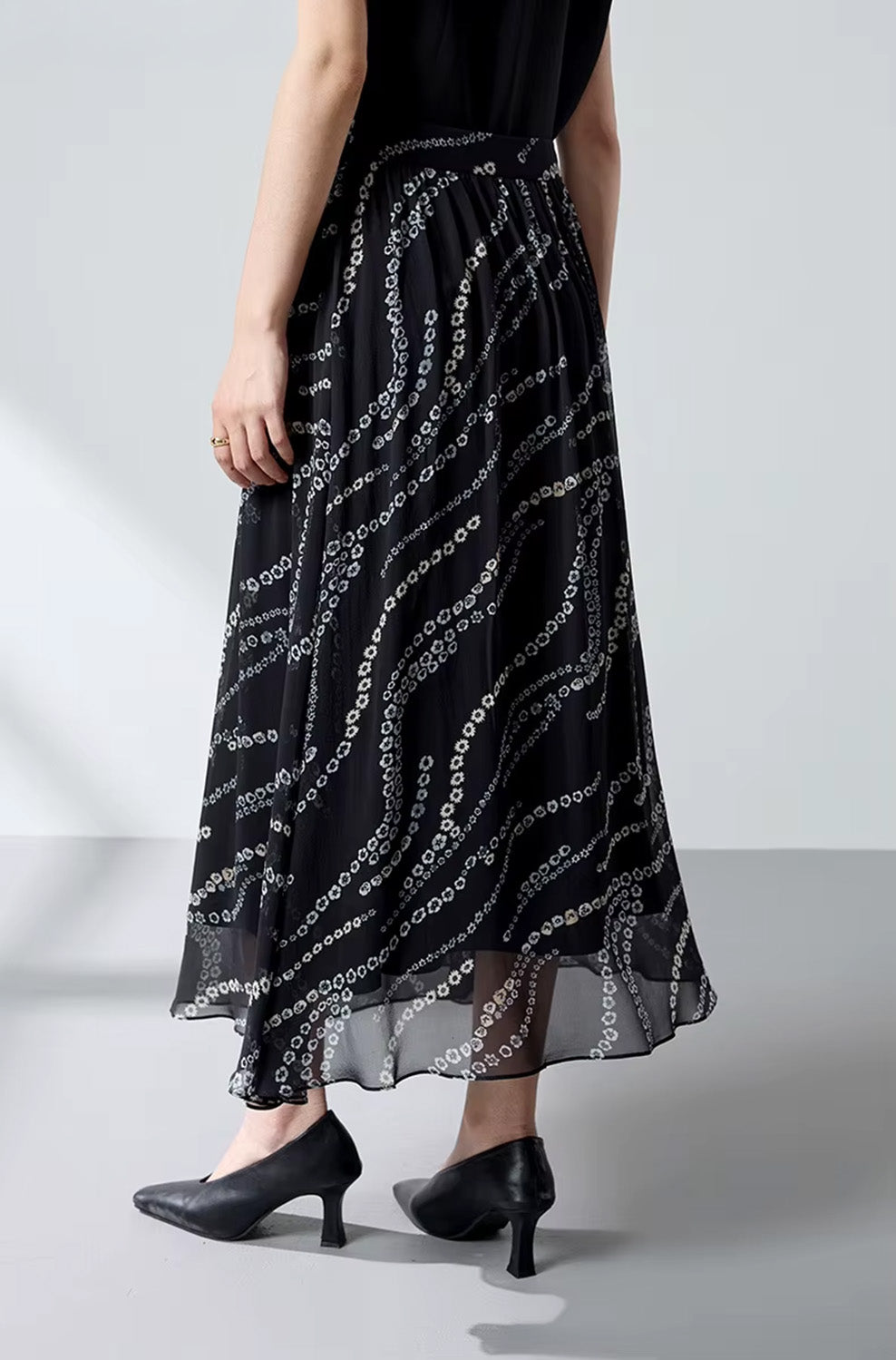 Back view of a model wearing a mid-calf black Mulberry silk skirt with a floral pattern — From Borcelleclothes.