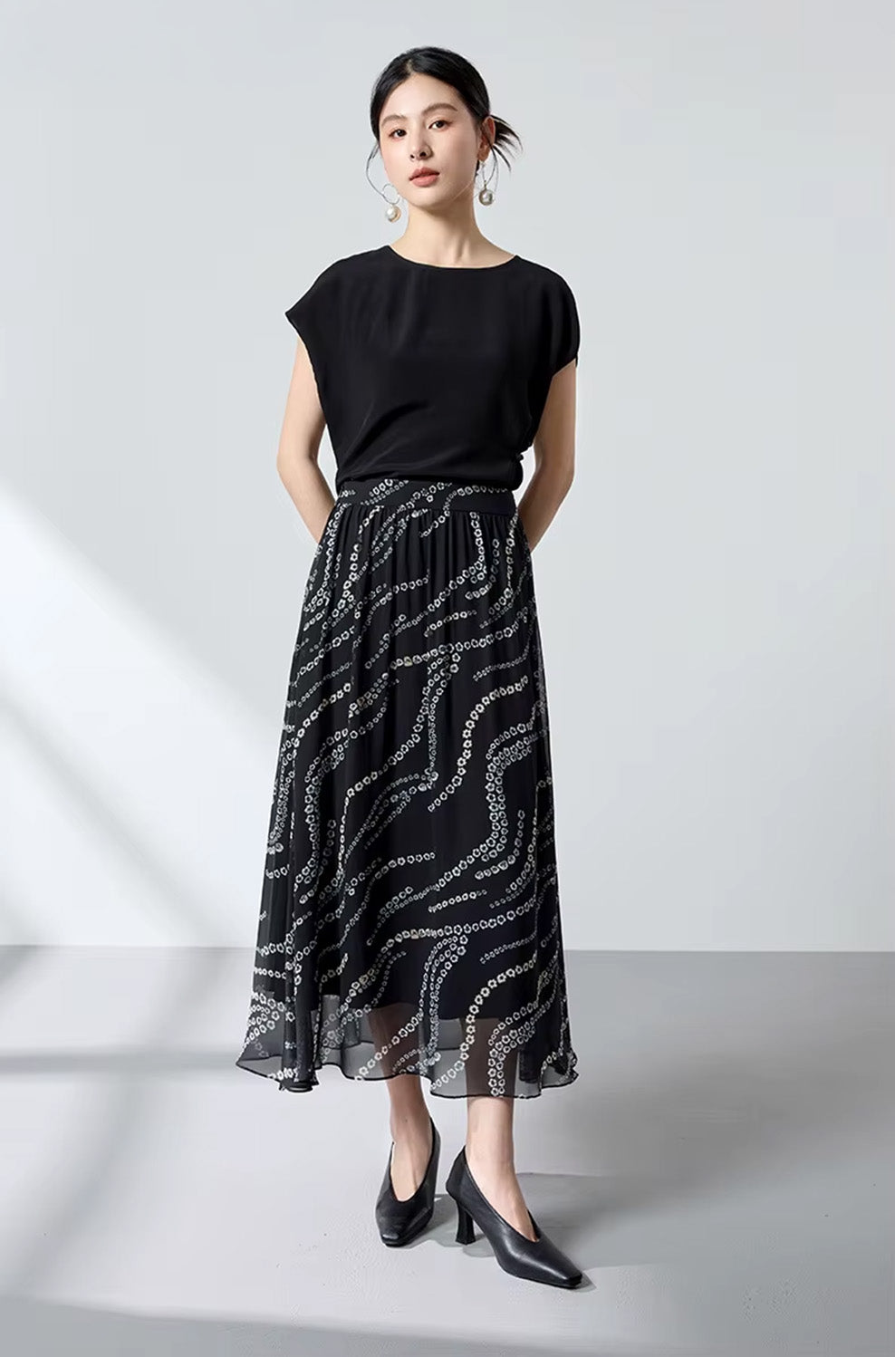 Full-height view of a model from behind, hands clasped behind her back, wearing a black silk georgette skirt — From Borcelleclothes.