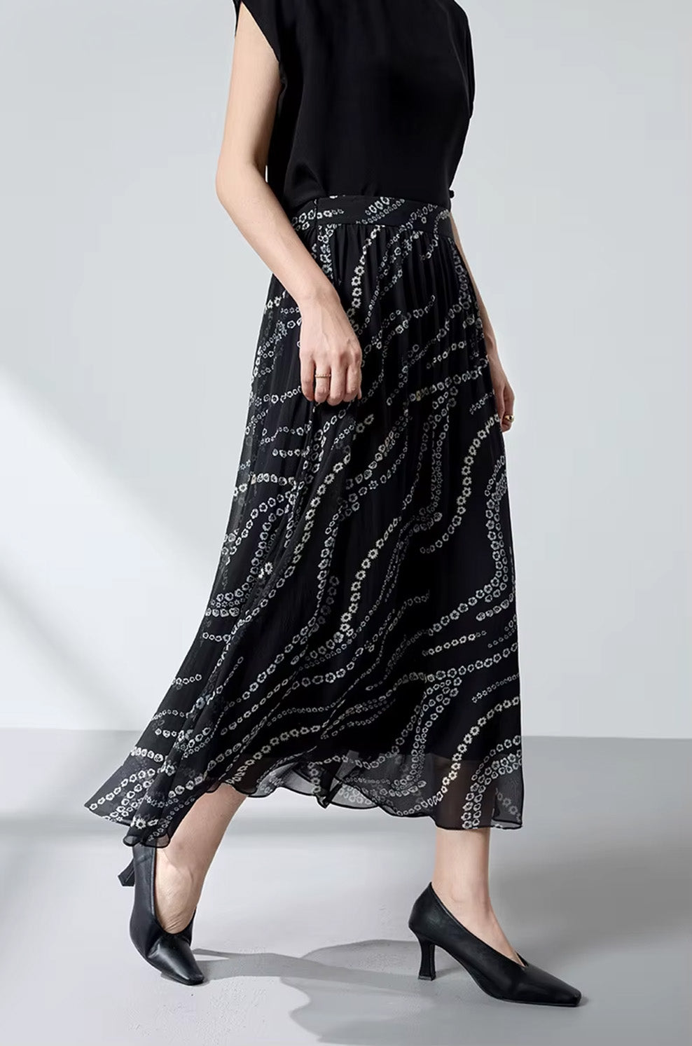 Side view of a model walking, demonstrating the fluid movement of a black silk georgette skirt — From Borcelleclothes.