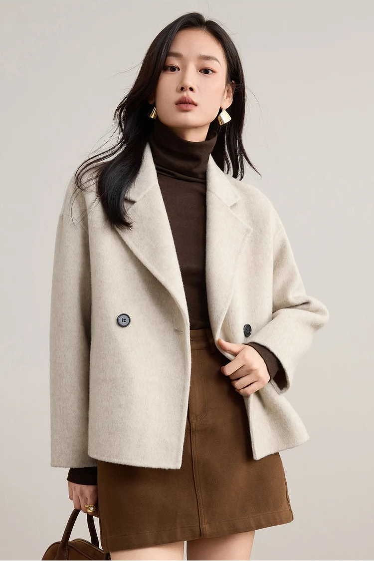 Close-up of a woman gently holding the front edge of her unfastened Bohemian wool jacket, showing the soft drape of the double-faced fabric. — From Borcelleclothes.