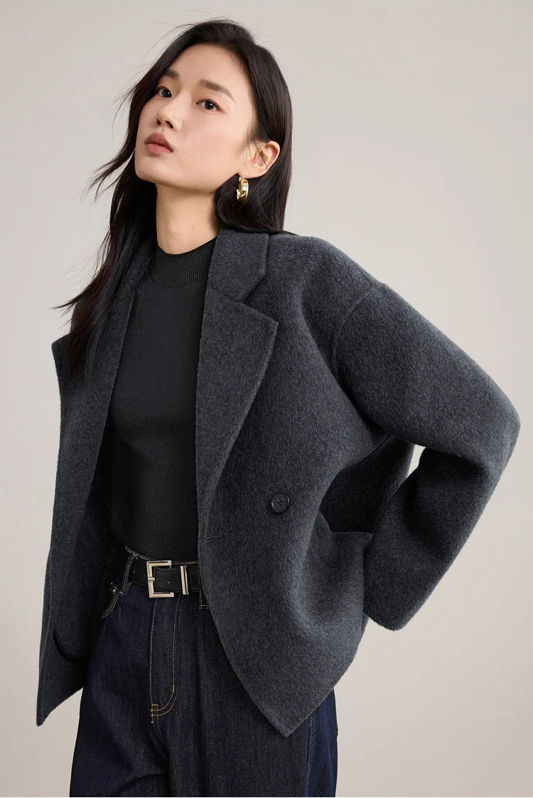 A woman standing in an unfastened Pause in Dialogue wool jacket with her hands tucked behind her back, emphasizing a minimalist aesthetic. — From Borcelleclothes.