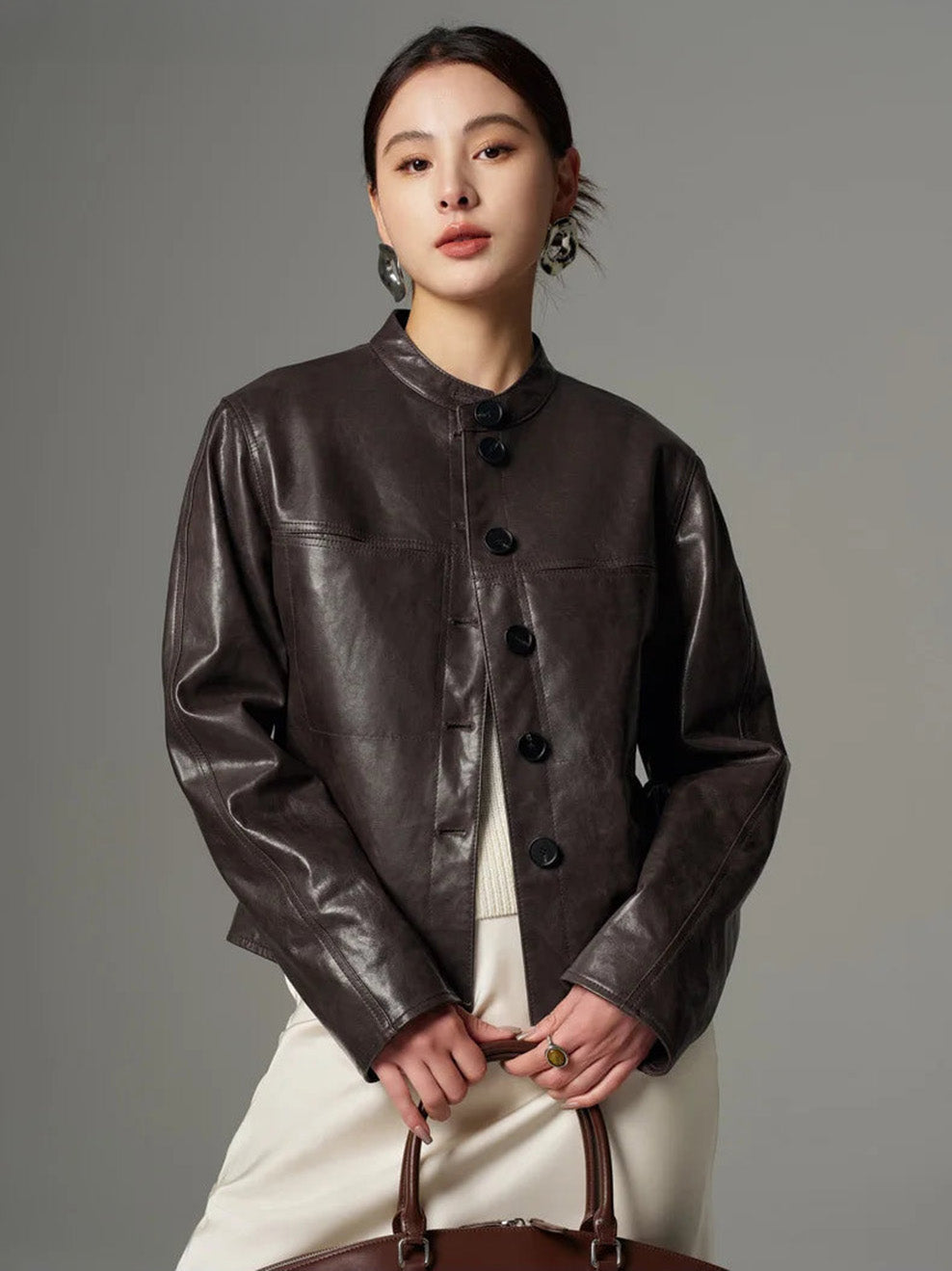 Model holding a structured bag with both hands while wearing the dark espresso waxed goatskin overshirt jacket — From Borcelleclothes.