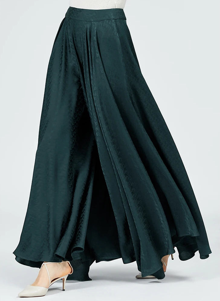 A woman walking in emerald green wide-leg palazzo trousers, viewed from the side. The high-quality mulberry silk jacquard fabric drapes gracefully with her movement. — From Borcelleclothes.