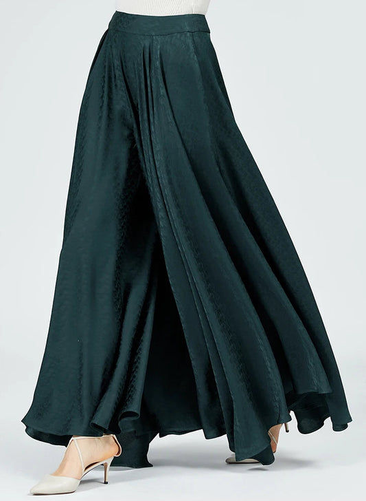 A woman walking in emerald green wide-leg palazzo trousers, viewed from the side. The high-quality mulberry silk jacquard fabric drapes gracefully with her movement. — From Borcelleclothes.