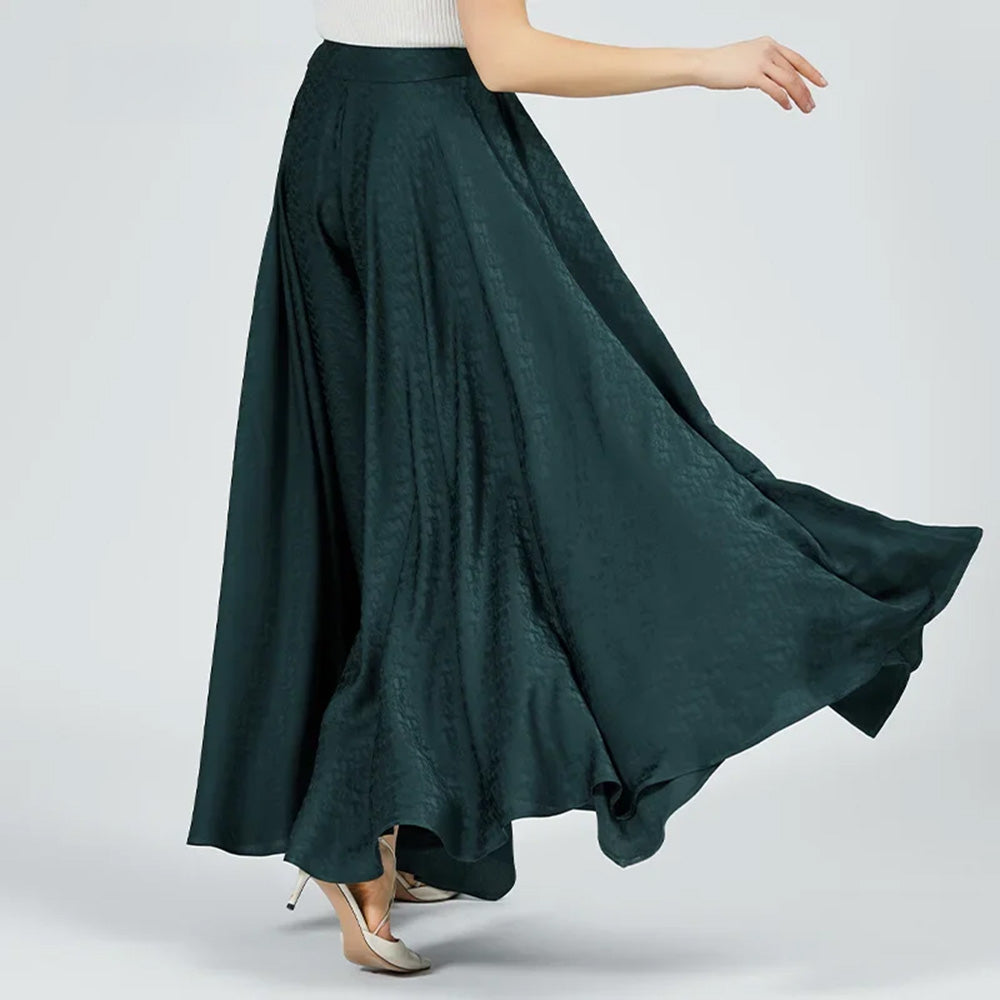 A woman viewed from the back while walking, showing the clean tailoring and the effortless flow of the floor-length emerald silk trousers. — From Borcelleclothes.