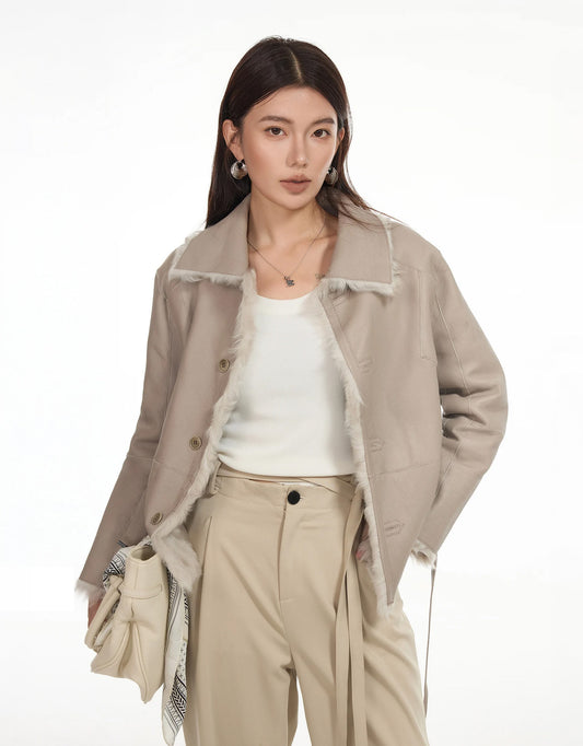 Woman wearing reversible shearling jacket in Oat Macchiato, leather side out, holding a bag — From Borcelleclothes.