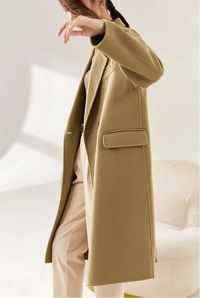 Alt Text: From Borcelleclothes: A model in the Do-Re-Mi sand-colored wool coat with a raised arm, showing the interaction of the structured wool with space and motion.