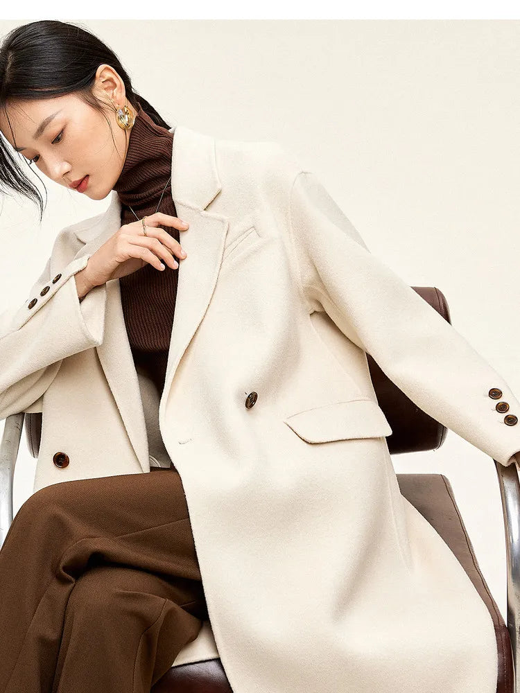 From Borcelleclothes: A model seated in the ivory Her Melody coat, gently touching the double-faced wool lapel to showcase its tangible density and hand-finished edges.