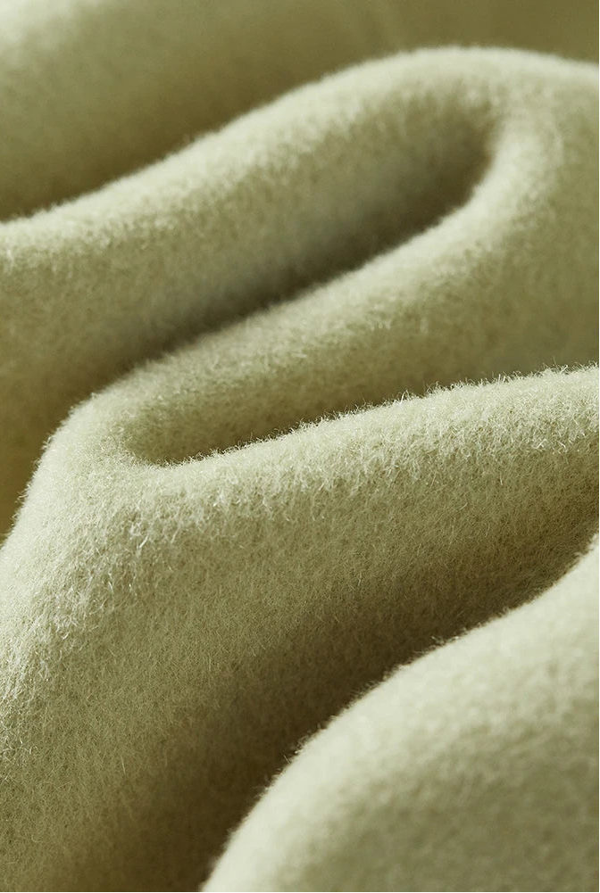 From Borcelleclothes: A detailed look at the Spring Staccato sage wool fabric, folded in a wave to highlight the 880g/m² density and the soft, tangible texture of 100% wool.