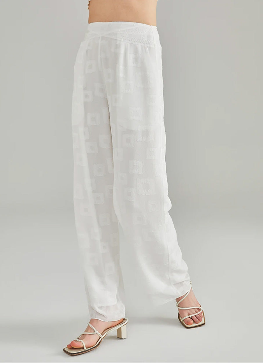 Side-motion view of a walking model demonstrating the fluid drape of floor-length white silk trousers — From Borcelleclothes.