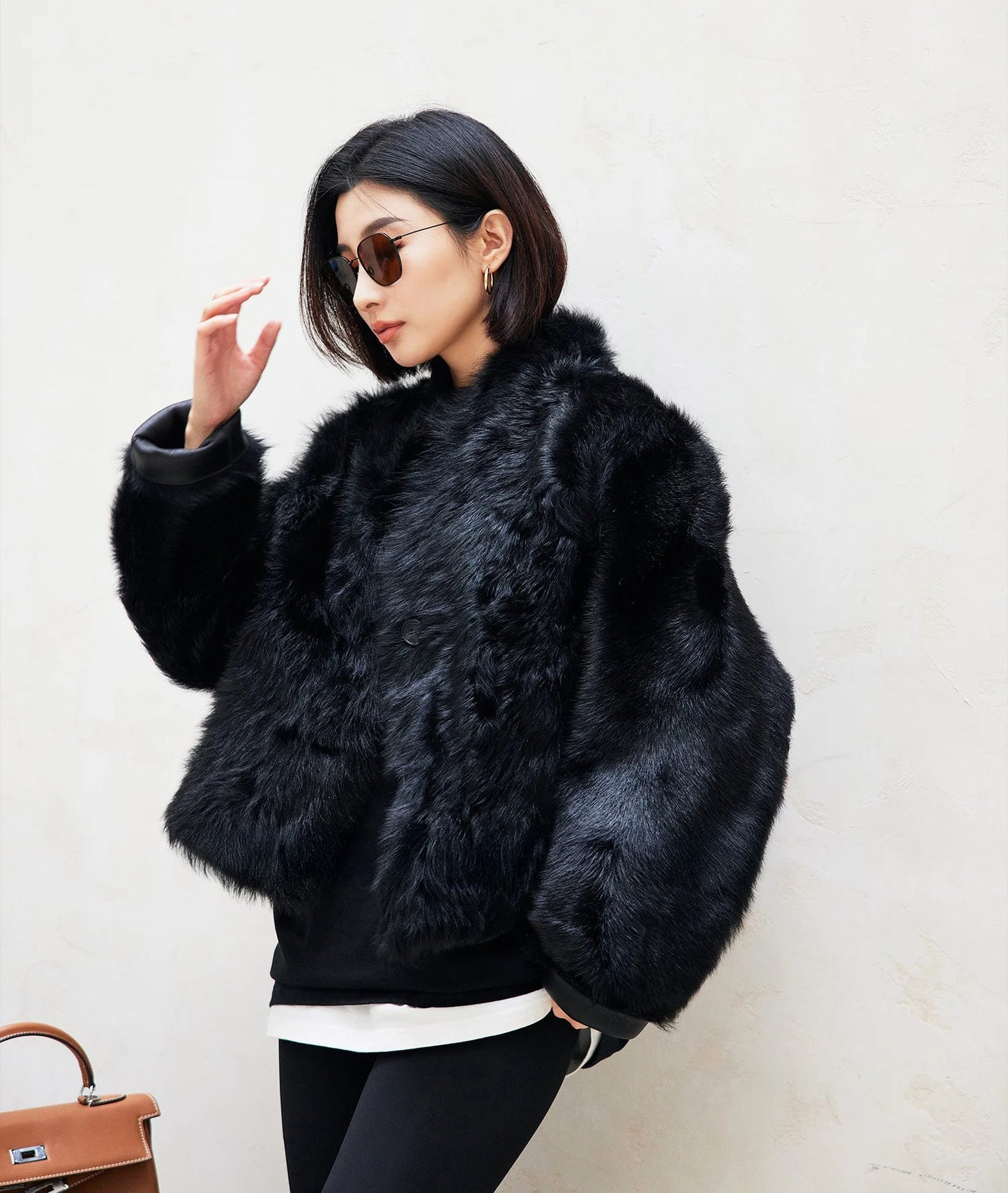 Model reaching to adjust sunglasses while wearing the Autographe reversible jacket, fur surface shown — From Borcelleclothes.