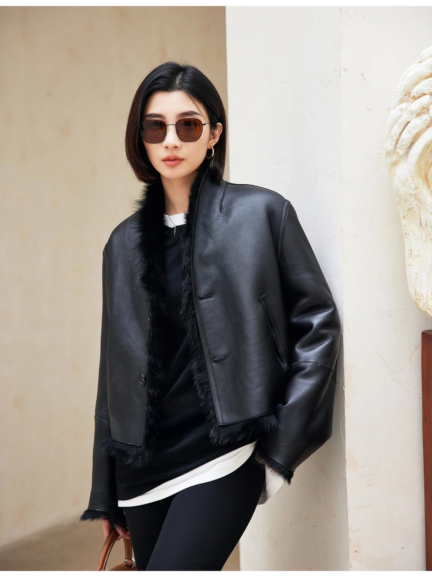 Model leaning against a wall in the unfastened Autographe shearling jacket, leather side out — From Borcelleclothes.