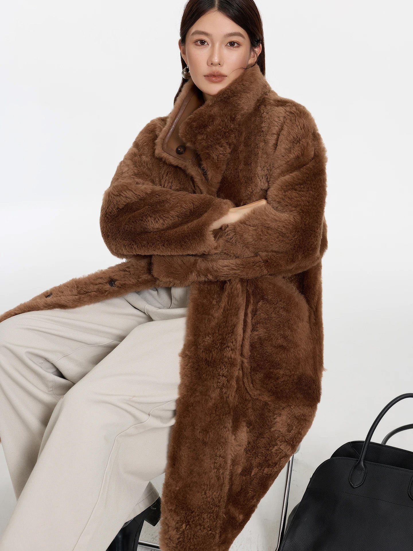 Model seated with arms crossed, wearing Cedar Resin shearling coat, fur side out — From Borcelleclothes.