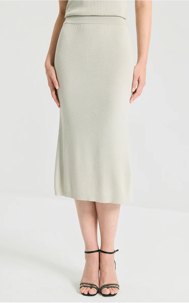 Model resting the hands on a sculptural 1x1 rib knit wool-silk blend skirt in Compliant Sage green. From Borcelleclothes.