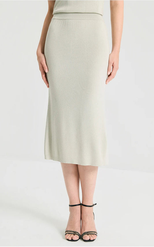 Model resting the hands on a sculptural 1x1 rib knit wool-silk blend skirt in Compliant Sage green. From Borcelleclothes.